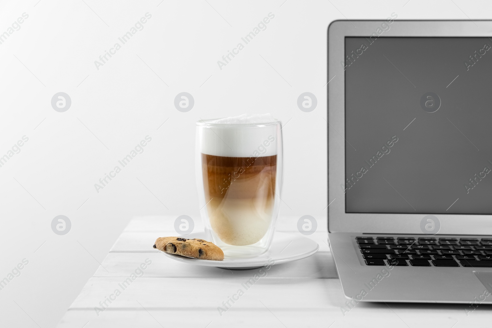 Photo of Chocolate chip cookie, latte and laptop on white wooden table indoors