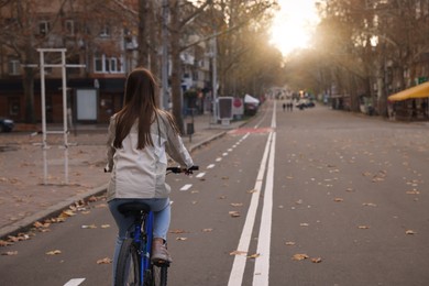 Photo of Woman riding bicycle on lane in city, back view