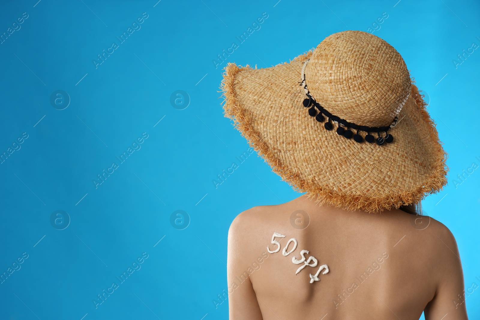 Photo of 50 SPF written with sun protection cream on woman's back against light blue background. Space for text