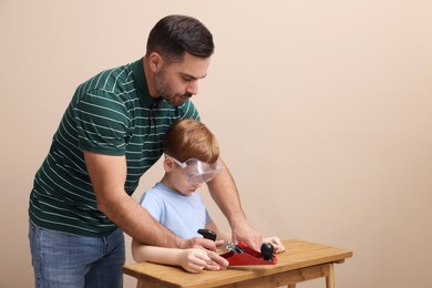 Photo of Father teaching son how to work with plane near beige wall