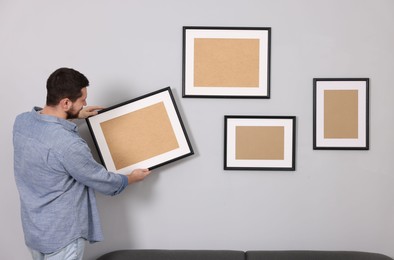 Man hanging picture frame on gray wall indoors
