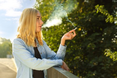 Photo of Woman smoking cigarette near railing outdoors on sunny day