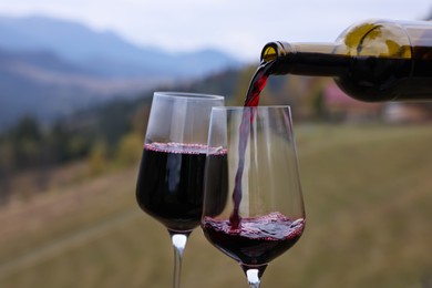 Pouring red wine into glass in mountains, closeup