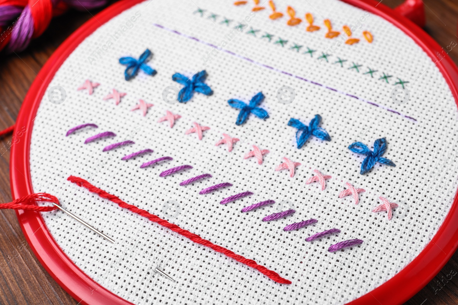 Photo of Fabric with colorful stitches and needle in embroidery hoop on wooden table, closeup