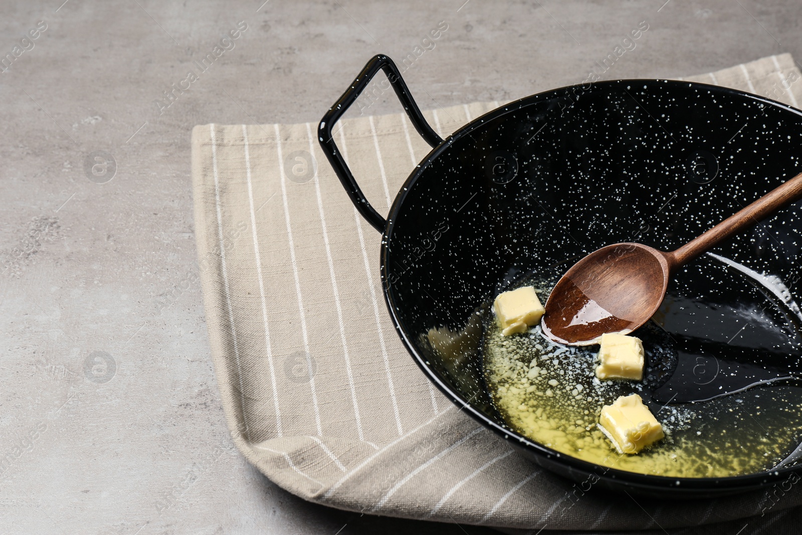 Photo of Frying pan with melting butter and wooden spoon on grey table. Space for text