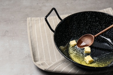 Frying pan with melting butter and wooden spoon on grey table. Space for text
