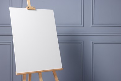 Wooden easel with blank canvas near grey wall indoors, closeup. Space for text