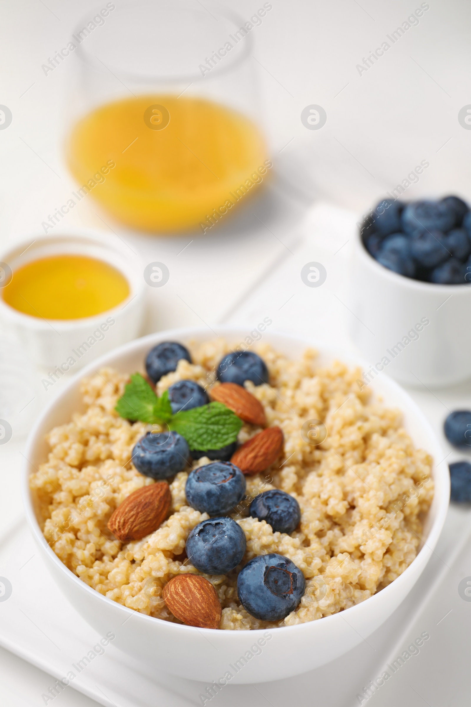 Photo of Bowl of delicious cooked quinoa with almonds and blueberries on white table, closeup