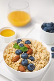 Photo of Bowl of delicious cooked quinoa with almonds and blueberries on white table, closeup