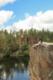 Photo of Young woman on rock near lake and forest. Camping season