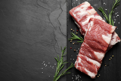 Raw ribs with rosemary and spices on black table, top view. Space for text