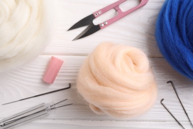 Photo of Felting wool, scissors and needles on white wooden table, flat lay