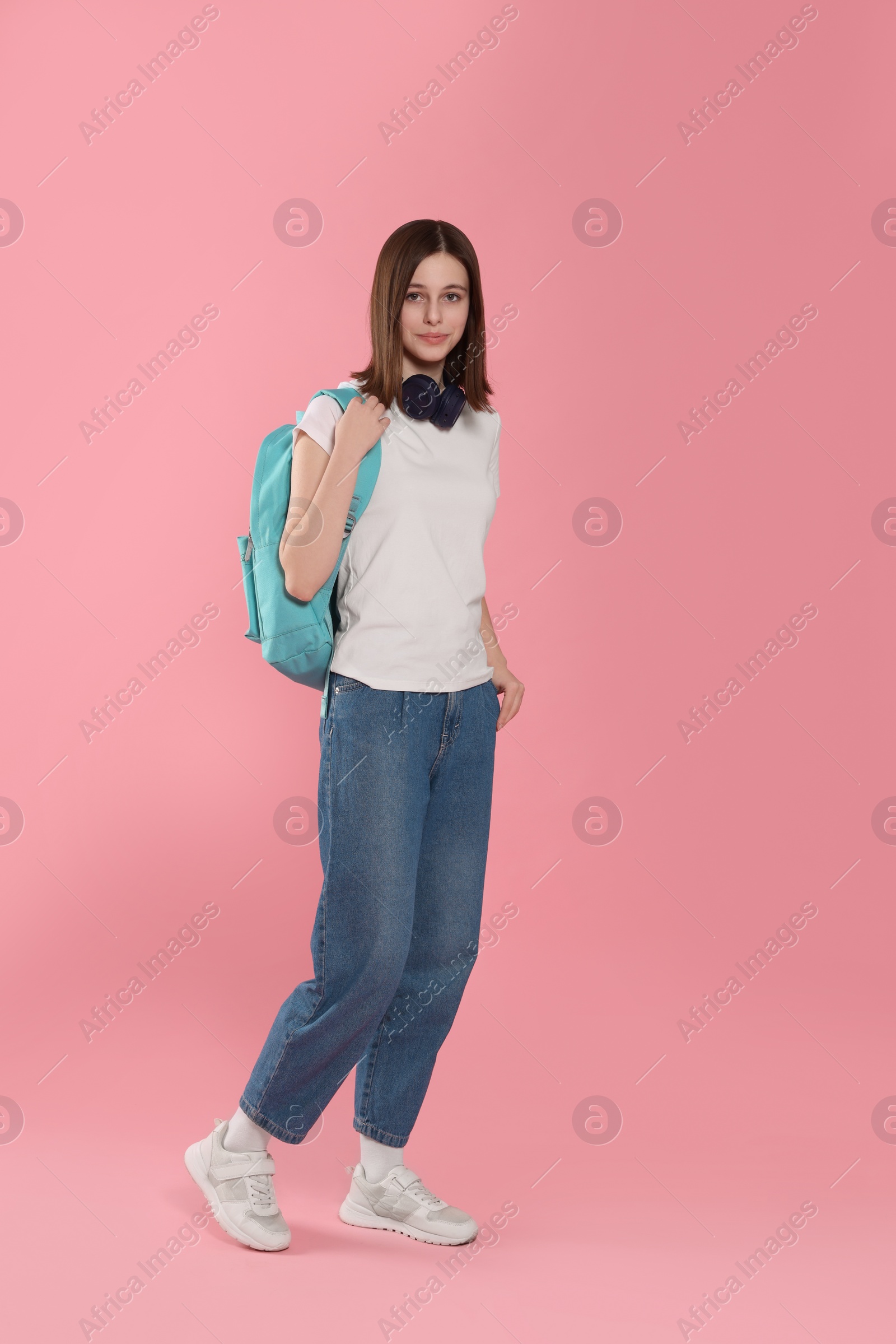 Photo of Cute teenage girl with headphones and backpack on pink background