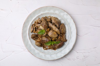 Photo of Plate of delicious fried chicken liver with onion and basil on white textured table, top view