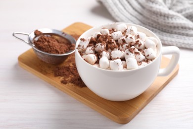 Cup of aromatic hot chocolate with marshmallows and cocoa powder on light wooden table, closeup