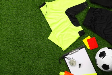 Uniform, soccer ball and other referee equipment on green grass, flat lay. Space for text