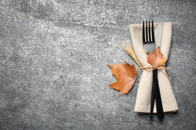 Photo of Cutlery and autumn leaves on grey background, top view with space for text. Thanksgiving Day celebration