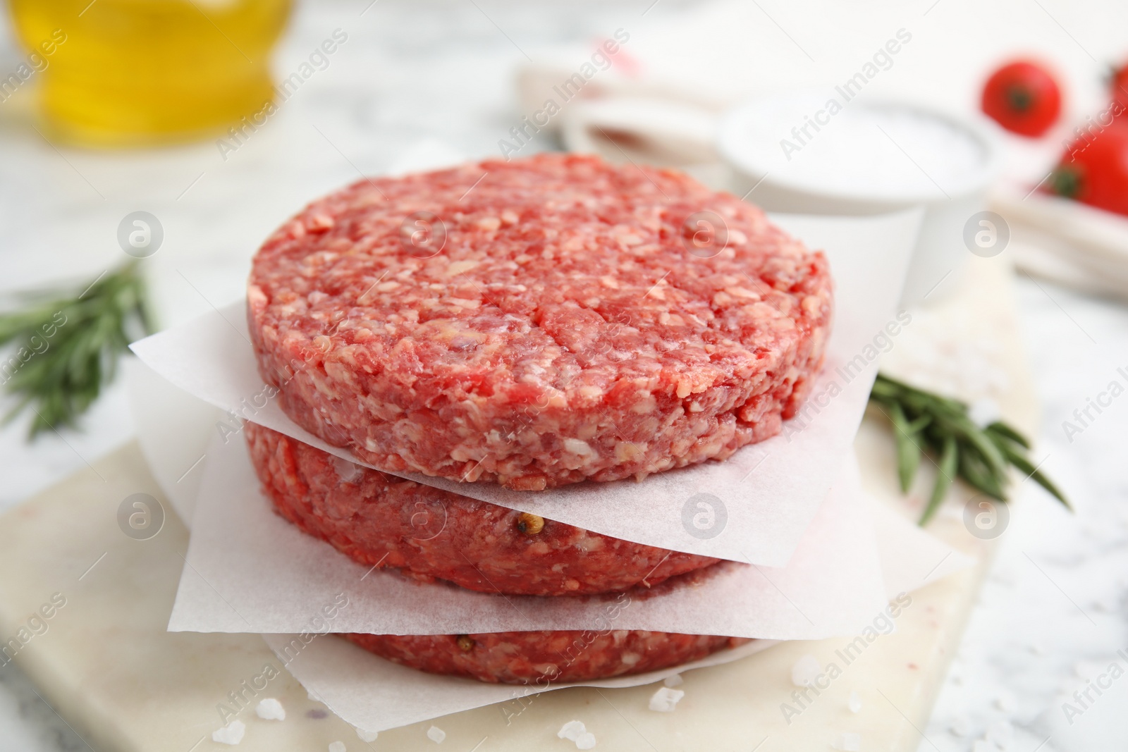 Photo of Raw hamburger patties with rosemary and salt on board, closeup