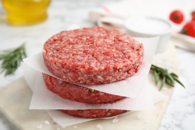 Raw hamburger patties with rosemary and salt on board, closeup