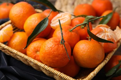 Photo of Fresh ripe tangerines with green leaves in wicker basket on table, closeup
