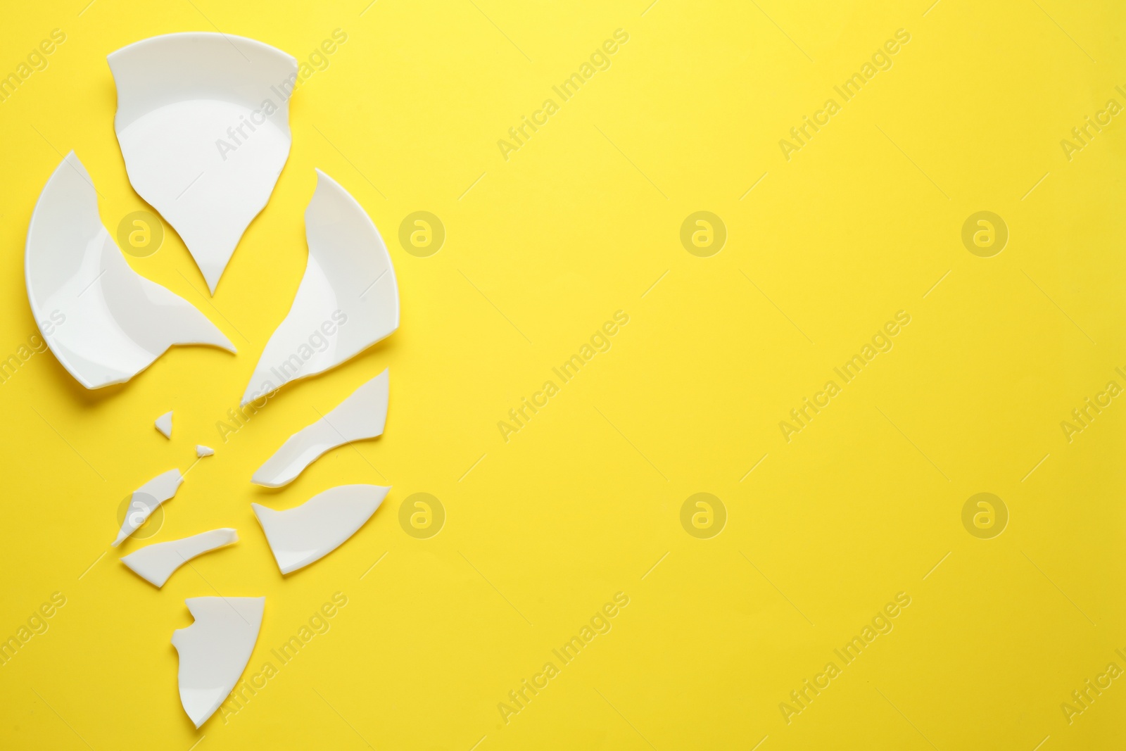 Photo of Pieces of broken ceramic plate on yellow background, flat lay. Space for text