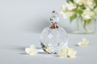 Photo of Aromatic perfume in bottle and beautiful jasmine flowers on grey background, closeup