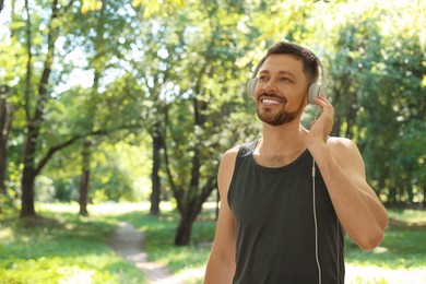 Handsome man with headphones on run in park, space for text. Morning exercise