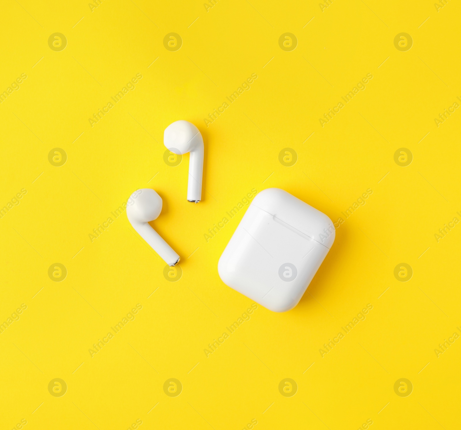 Photo of Modern wireless earphones and charging case on yellow background, flat lay