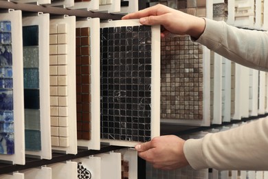 Photo of Man choosing tile among different samples in store, closeup