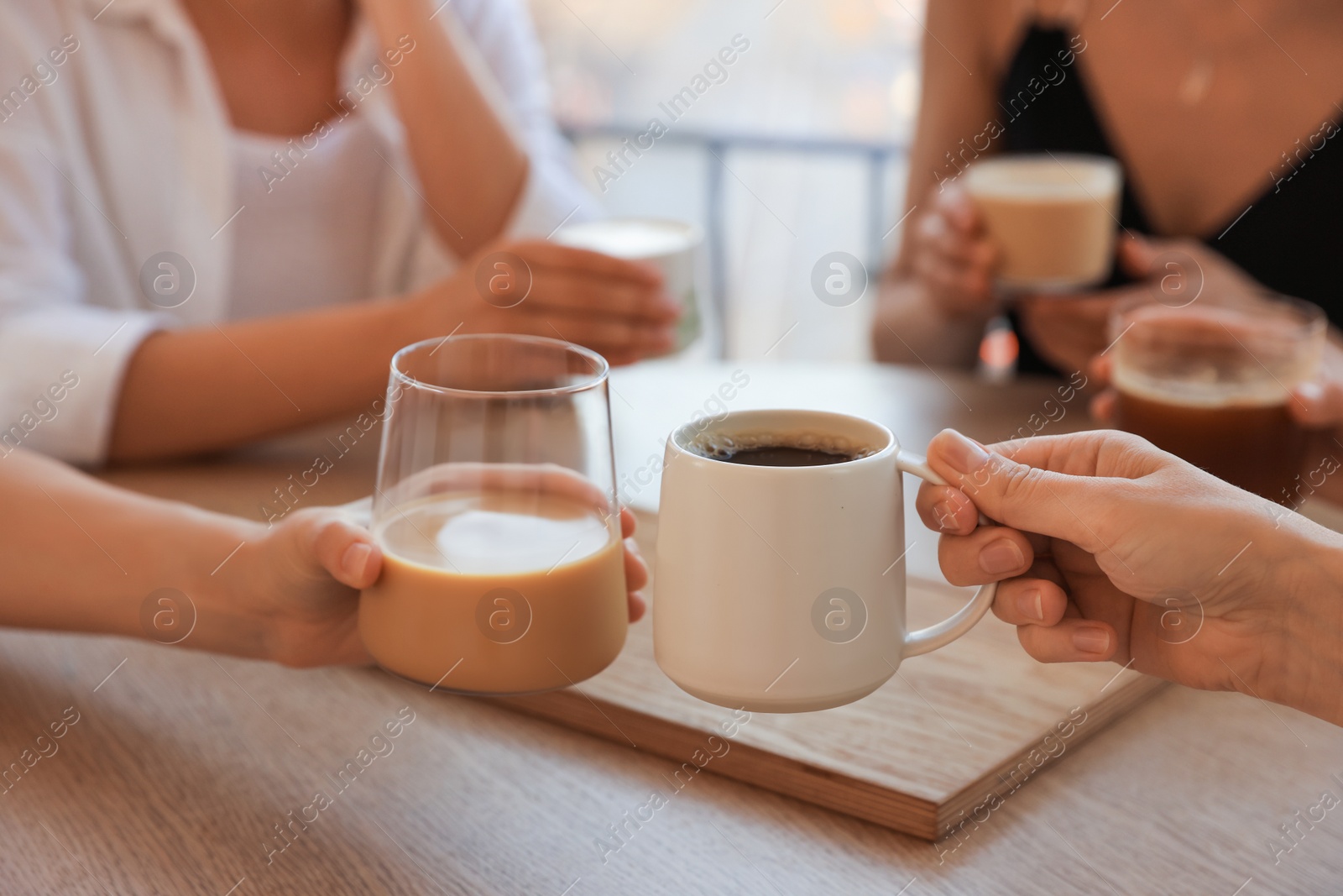 Photo of Friends drinking coffee at wooden table in cafe, closeup