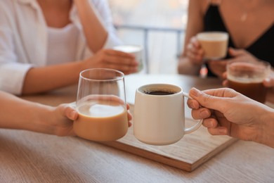 Friends drinking coffee at wooden table in cafe, closeup