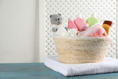 Photo of Wicker basket with different baby cosmetic products, bathing accessories and toy on light blue wooden table. Space for text