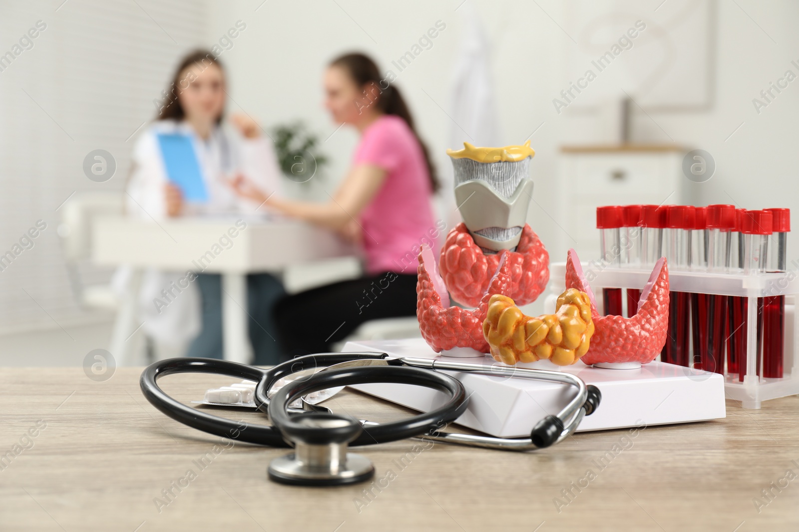 Photo of Endocrinologist examining patient at clinic, focus on stethoscope and model of thyroid gland