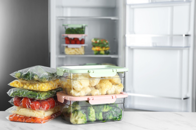 Different frozen vegetables on white marble table near open refrigerator