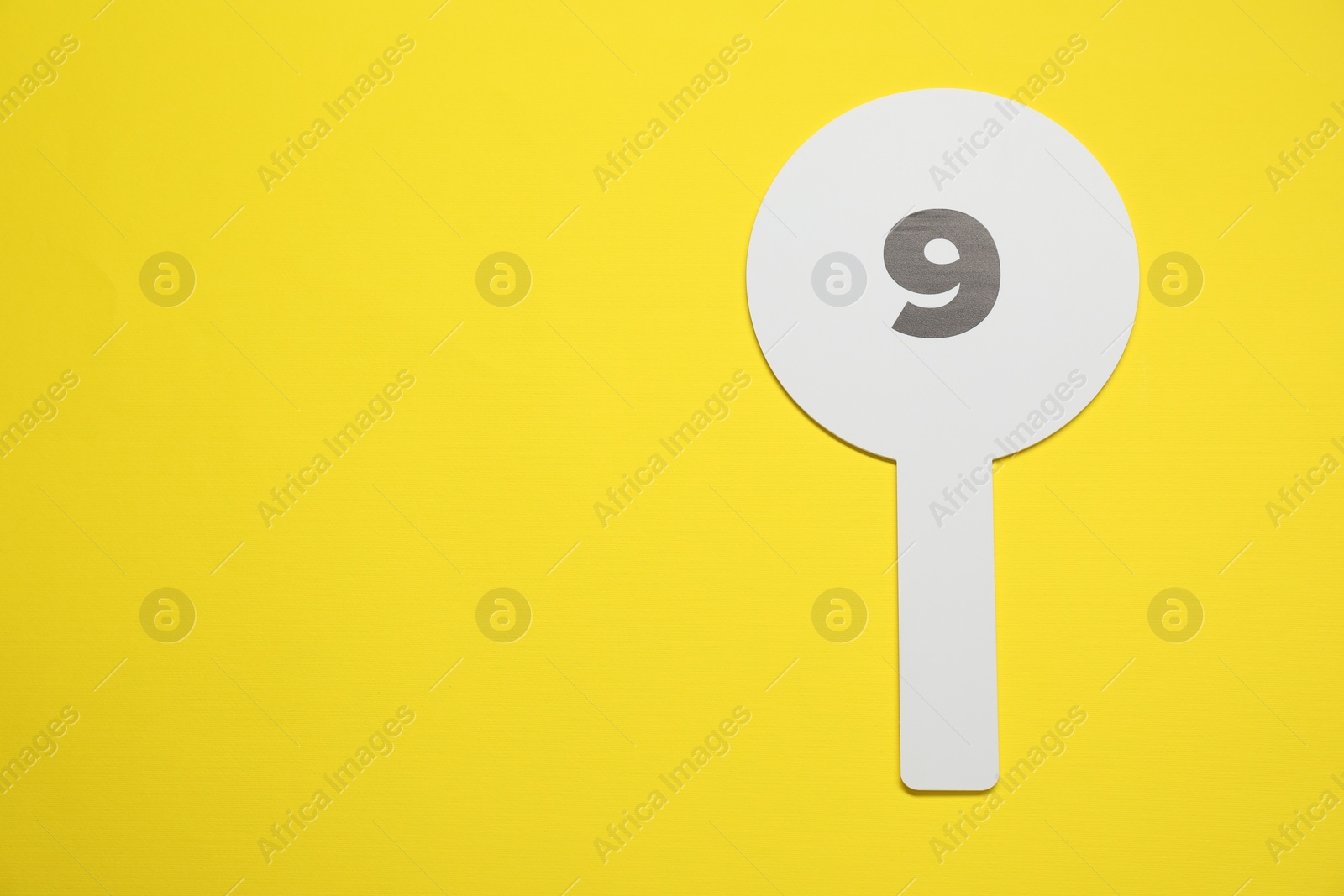 Photo of Auction paddle with number 9 on yellow background, top view. Space for text