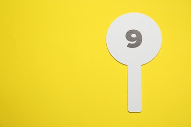 Photo of Auction paddle with number 9 on yellow background, top view. Space for text