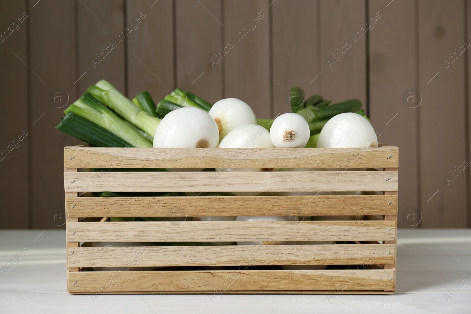 Photo of Crate with green spring onions on white wooden table