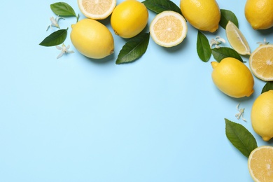 Many fresh ripe lemons with green leaves and flowers on light blue background, flat lay. Space for text
