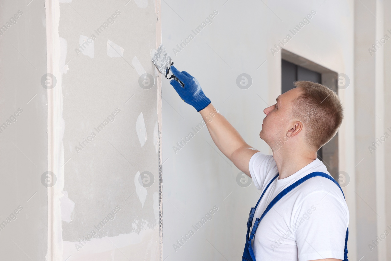 Photo of Man plastering wall with putty knife indoors. Home renovation