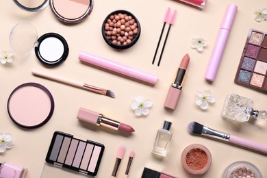 Flat lay composition with different makeup products and beautiful spring flowers on beige background