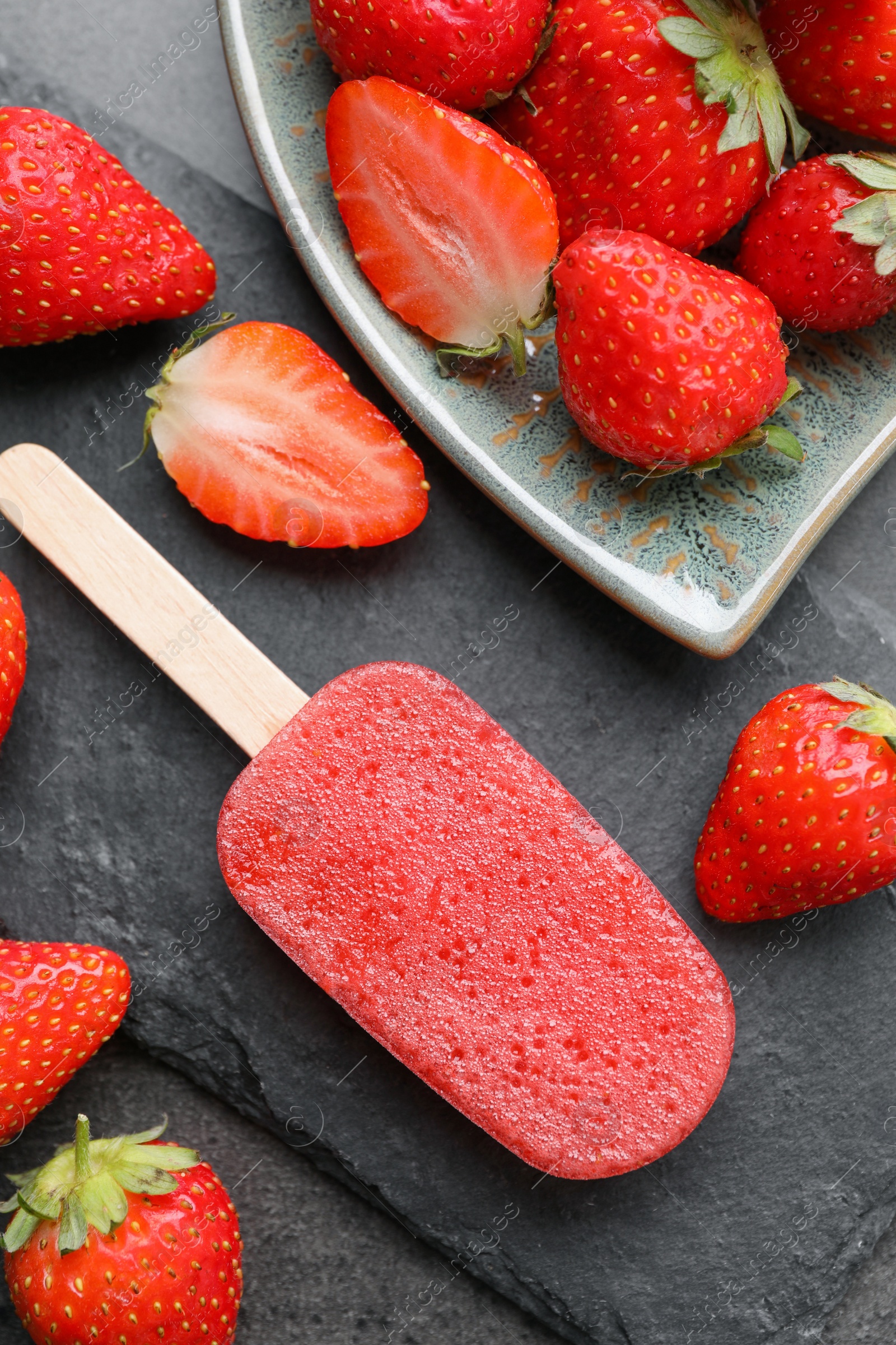 Photo of Tasty strawberry ice pop on dark table, flat lay. Fruit popsicle