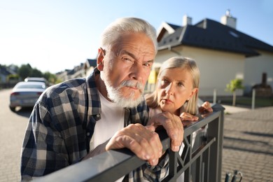 Photo of Concept of private life. Curious senior couple spying on neighbours over fence outdoors
