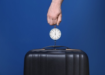 Photo of Man weighing stylish suitcase against color background, closeup