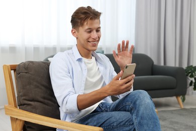 Photo of Happy young man having video chat via smartphone on armchair indoors