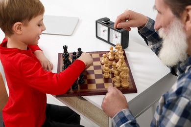 Photo of Grandfather and grandson playing chess at table indoors, closeup