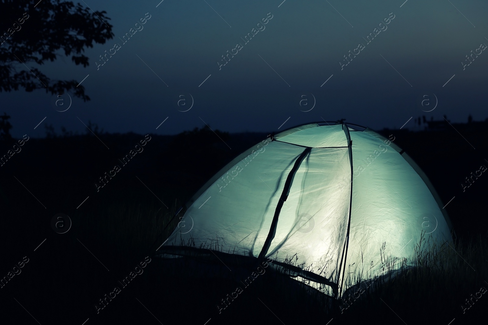 Photo of Small camping tent glowing in twilight outdoors. Space for text