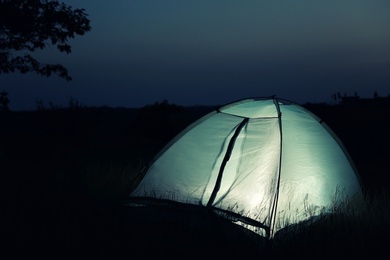 Small camping tent glowing in twilight outdoors. Space for text