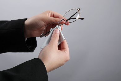 Photo of Woman wiping glasses with microfiber cloth on light grey background, closeup. Space for text