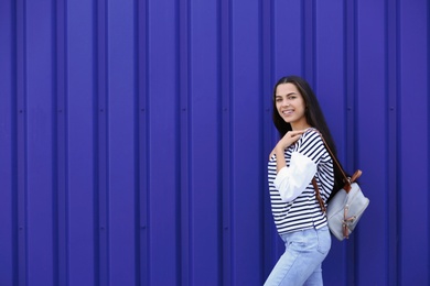 Photo of Young hipster woman in stylish jeans posing near color wall