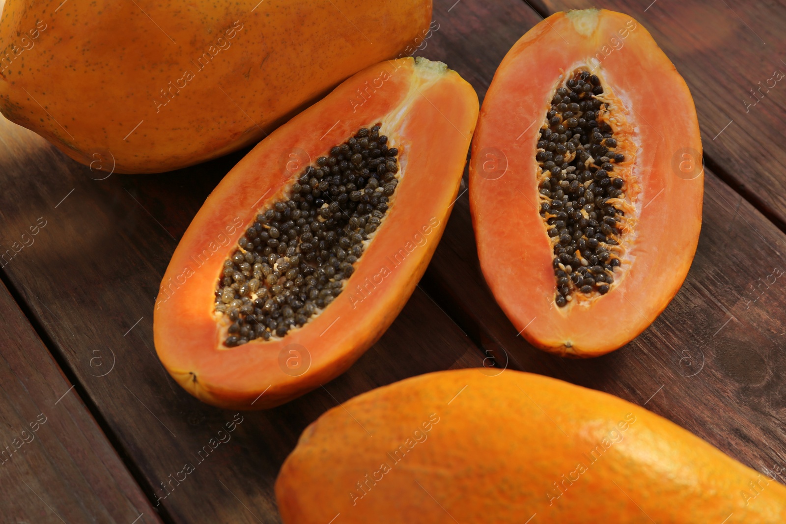 Photo of Fresh ripe cut and whole papaya fruits on wooden table, closeup